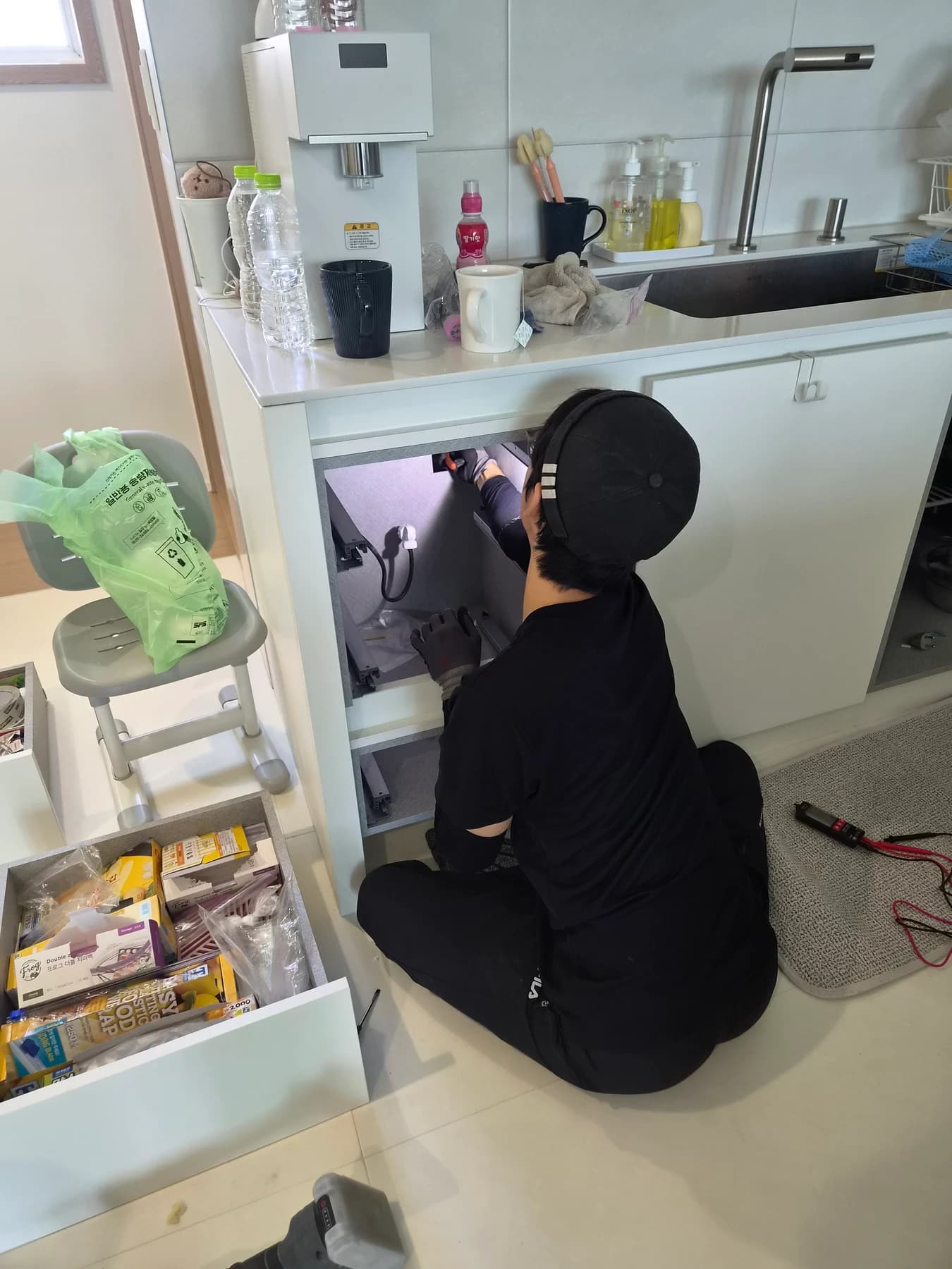 서랍을 꺼낸 주방 수납장 안쪽 접속부를 살피는 작업자